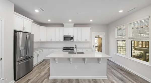 a kitchen with stainless steel appliances granite countertop a stove a refrigerator a sink and white cabinets with wooden floor