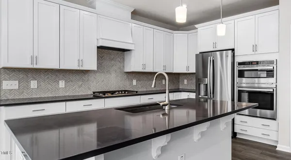 a kitchen with stainless steel appliances granite countertop a sink a stove and a refrigerator with white cabinets