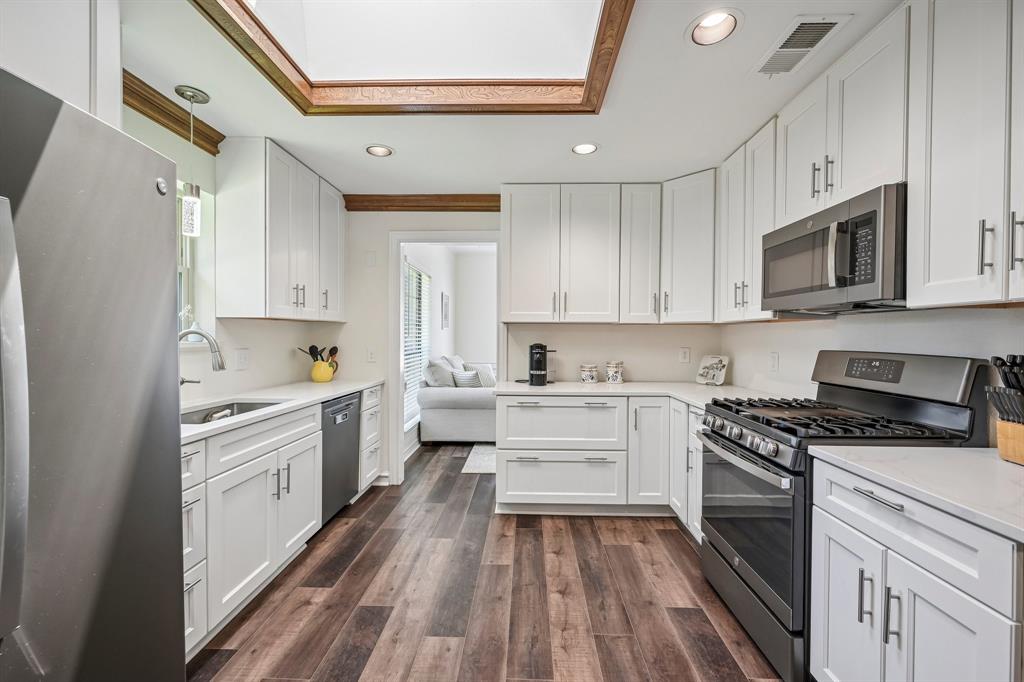 925 Spring Brook Drive Allen, TX 75002 - Photo 12 of 30 Kitchen featuring wood-finish flooring, white cabinetry, integrated stainless steel appliances, light countertops, and a recessed ceiling with wood trim
