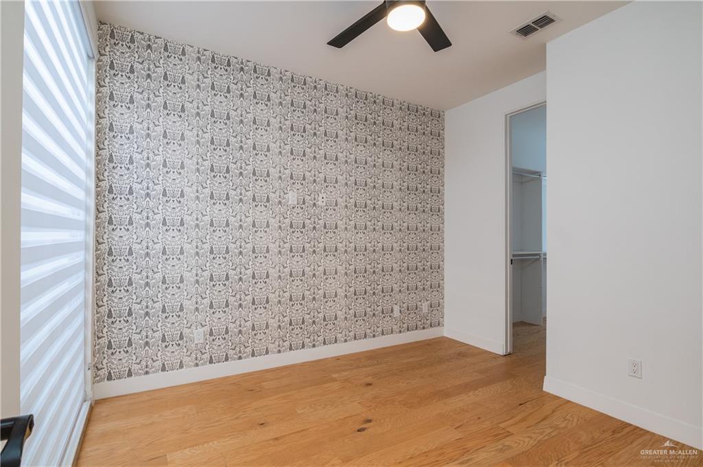 915 Santa Lucia Street Mission, TX 78572 - Photo 12 of 23 Unfurnished bedroom with a walk in closet, wood finished floors, an accent wall, and a ceiling fan