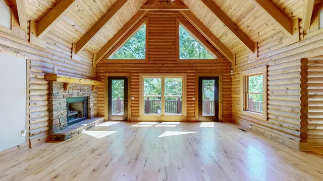 a view of an empty room with wooden floor fire place and windows