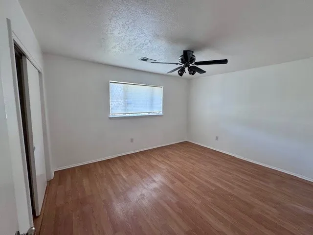 an empty room with wooden floor ceiling fan and window