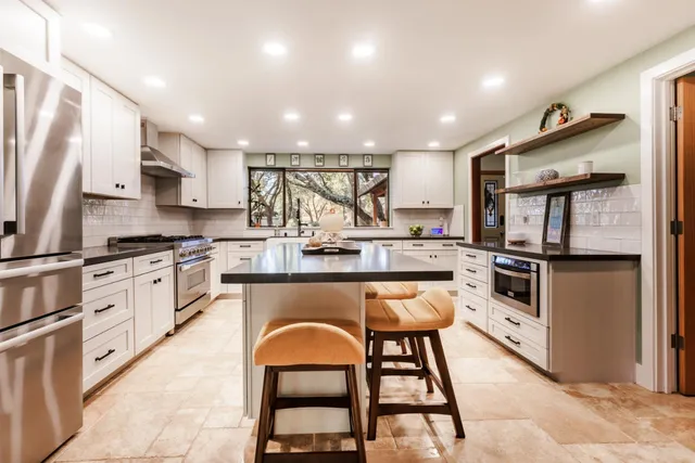 a kitchen with stainless steel appliances kitchen island granite countertop a table chairs sink and cabinets