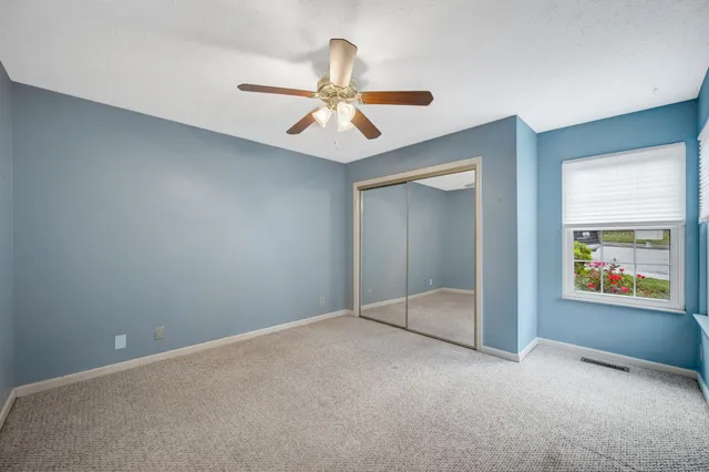 an empty room with chandelier fan and windows