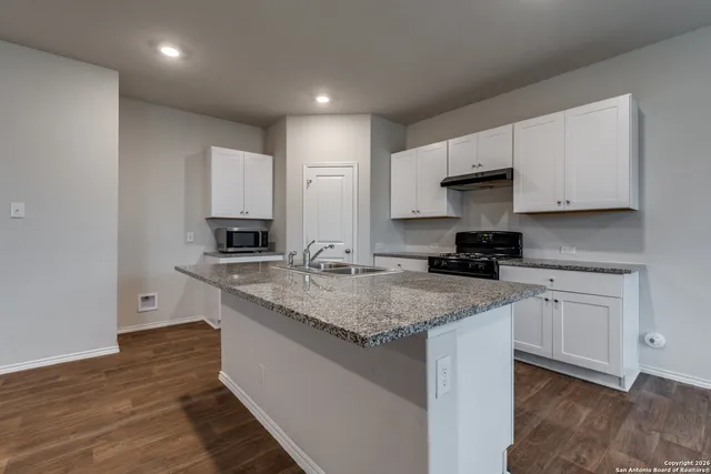 a kitchen with stainless steel appliances granite countertop a sink stove and white cabinets with wooden floor