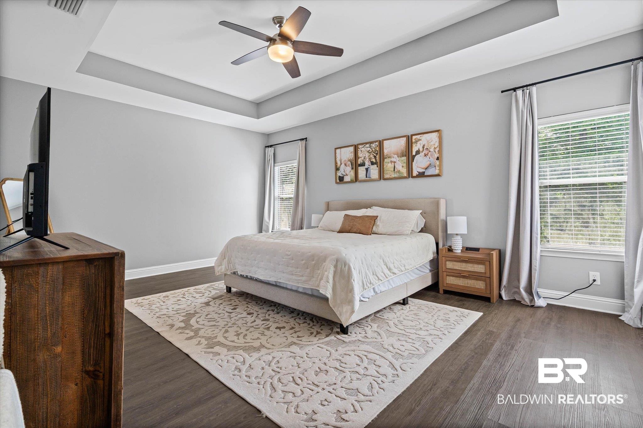 3739 Whitestone Drive Semmes, AL 36575 - Photo 12 of 25 Spacious bedroom featuring a tray ceiling with a ceiling fan, dark wood-finish flooring, light grey walls, and a large window with blinds and curtains
