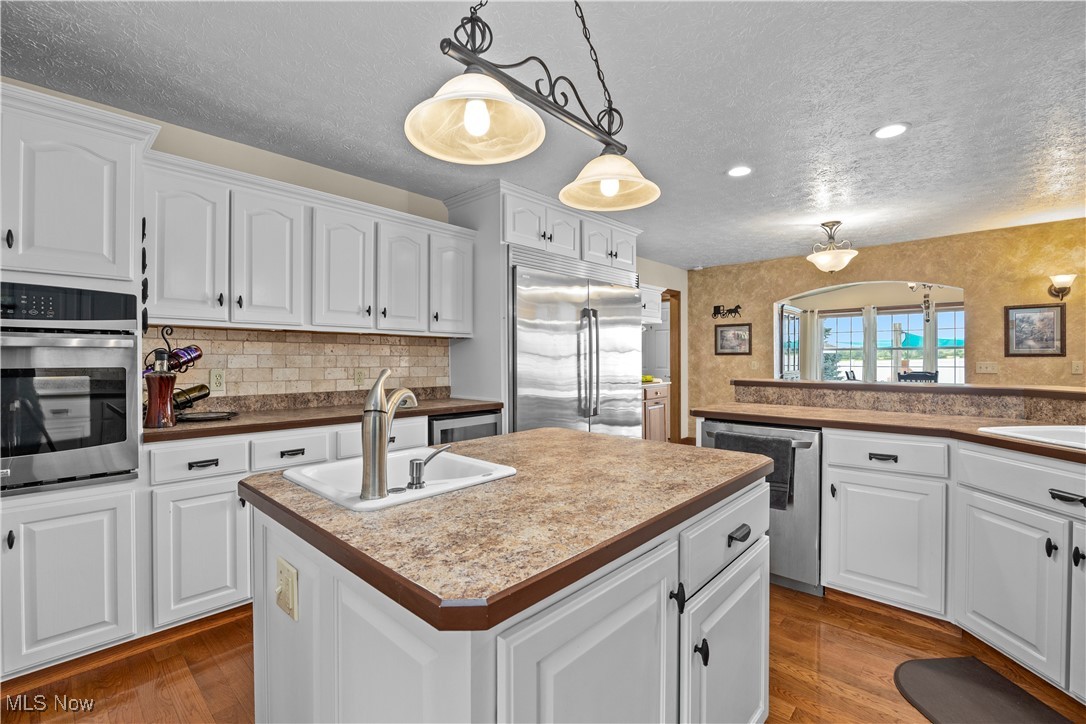 47147 Merriam Road Wellington, OH 44090 - Photo 18 of 49 Kitchen with stainless steel appliances, a textured ceiling, a center island with prep sink, white cabinetry, and dark wood flooring