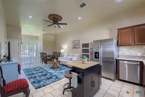 a kitchen with stainless steel appliances kitchen island granite countertop a table chairs and a refrigerator