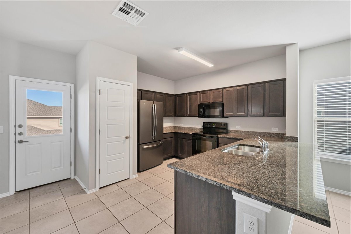 1202 Garland Road Georgetown, TX 78626 - Photo 4 of 28 Kitchen featuring dark wood cabinetry, a stainless steel refrigerator, black appliances, and a granite-finish countertop with an undermount sink