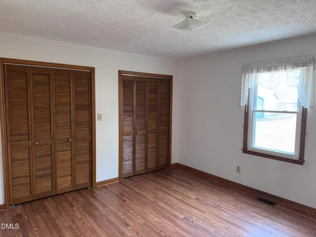 an empty room with wooden floor closet and windows