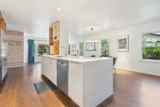 a living room with stainless steel appliances kitchen island wooden floor and large windows