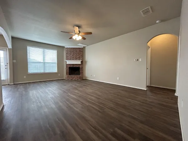 an empty room with wooden floor chandelier fan and windows