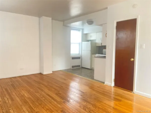 a view of empty room with wooden floor and kitchen