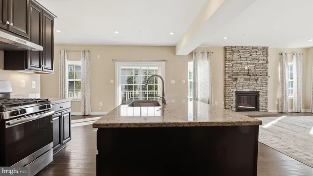 a open kitchen with granite countertop a stove top oven a sink dishwasher and a fireplace with wooden floor