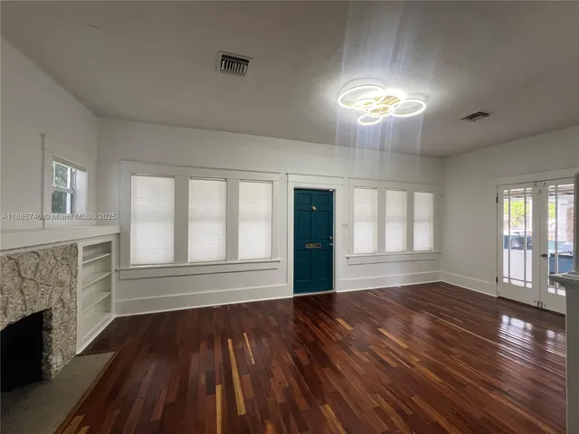 a view of an empty room with wooden floor fireplace and a window