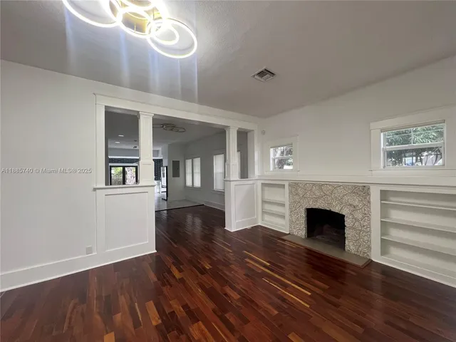 a view of an empty room with wooden floor fireplace and a window
