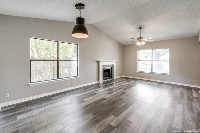 an empty room with wooden floor chandelier and windows
