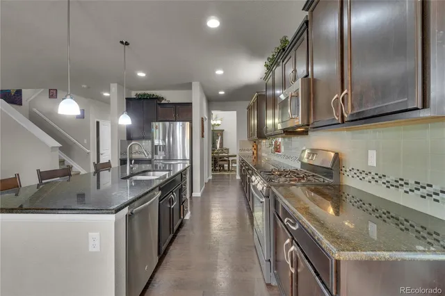 a kitchen with stainless steel appliances granite countertop a sink a stove and a wooden floors