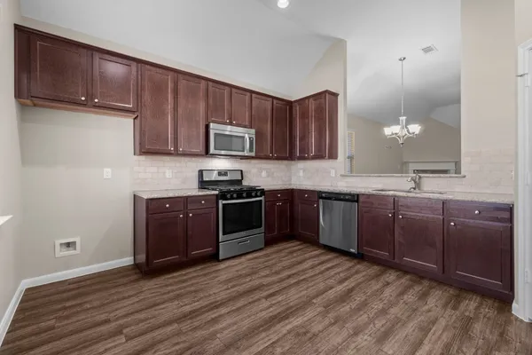 a kitchen with stainless steel appliances kitchen island granite countertop a stove a sink dishwasher and a refrigerator with wooden floor