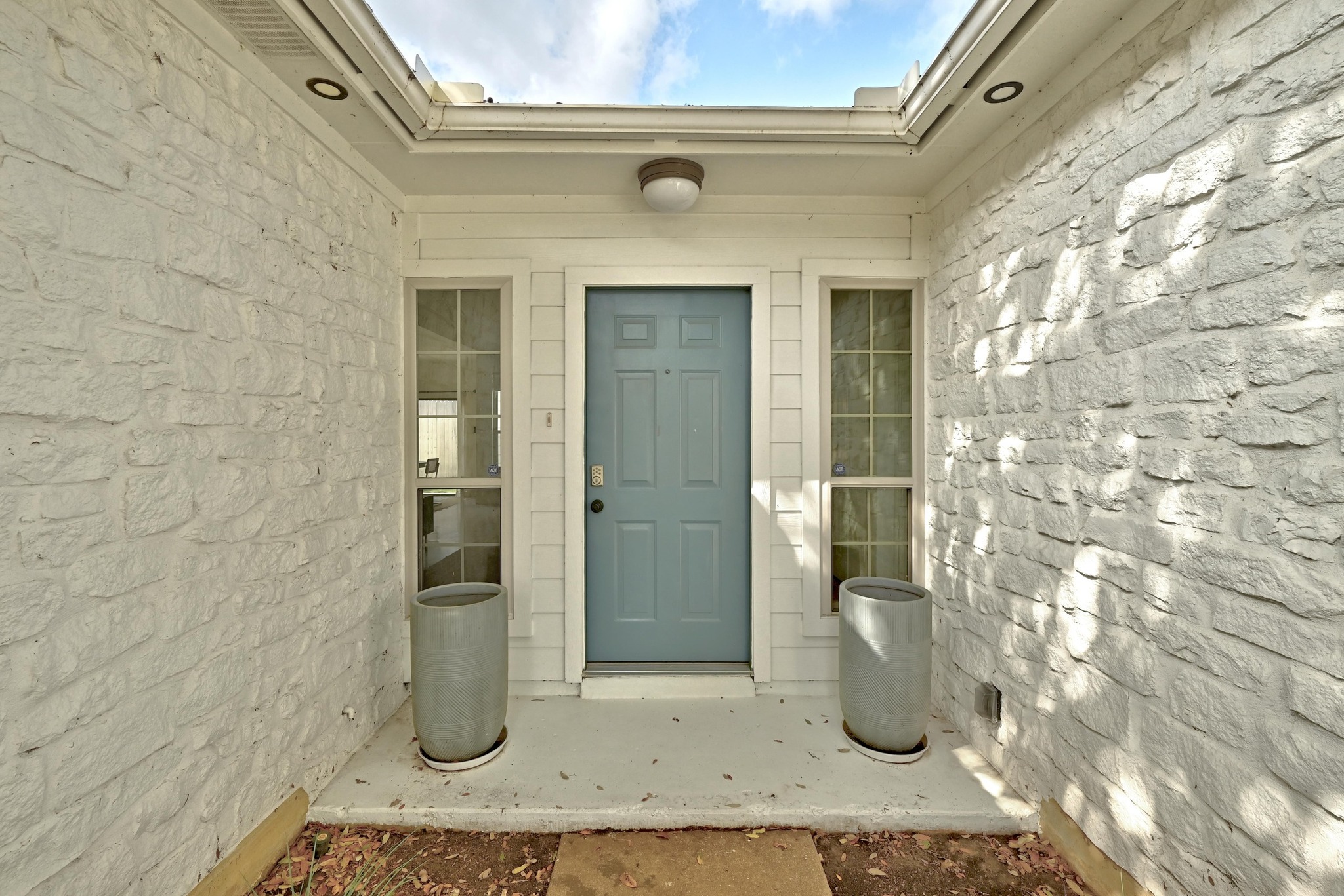 5807 Convict Hill Road Austin, TX 78749 - Photo 3 of 27 The inviting front entry features a cheerful blue door nestled between twin sidelight windows, framed by textured white stone walls. This welcoming vignette sets the tone for a home that blends style and warmth.
