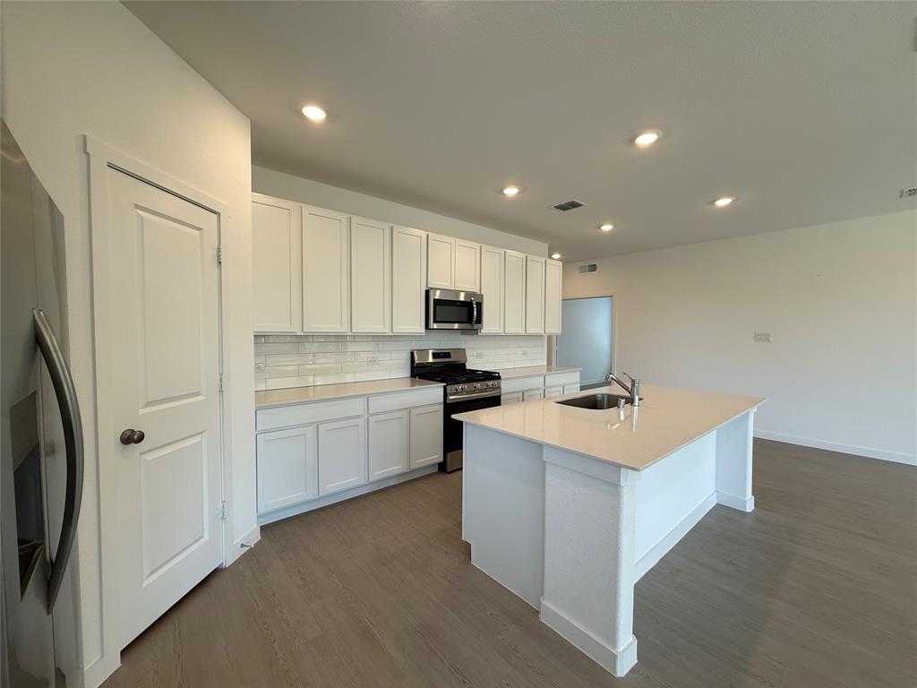 3025 Timber Rdg Drive Anna, TX 75409 - Photo 7 of 23 Open-concept kitchen featuring white cabinetry, stainless steel appliances, a center island with an integrated sink, recessed lighting, and wood-finish flooring