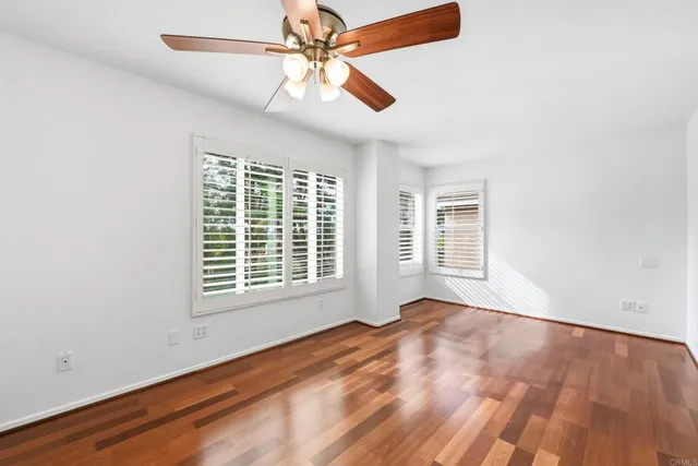 an empty room with wooden floor fan and windows