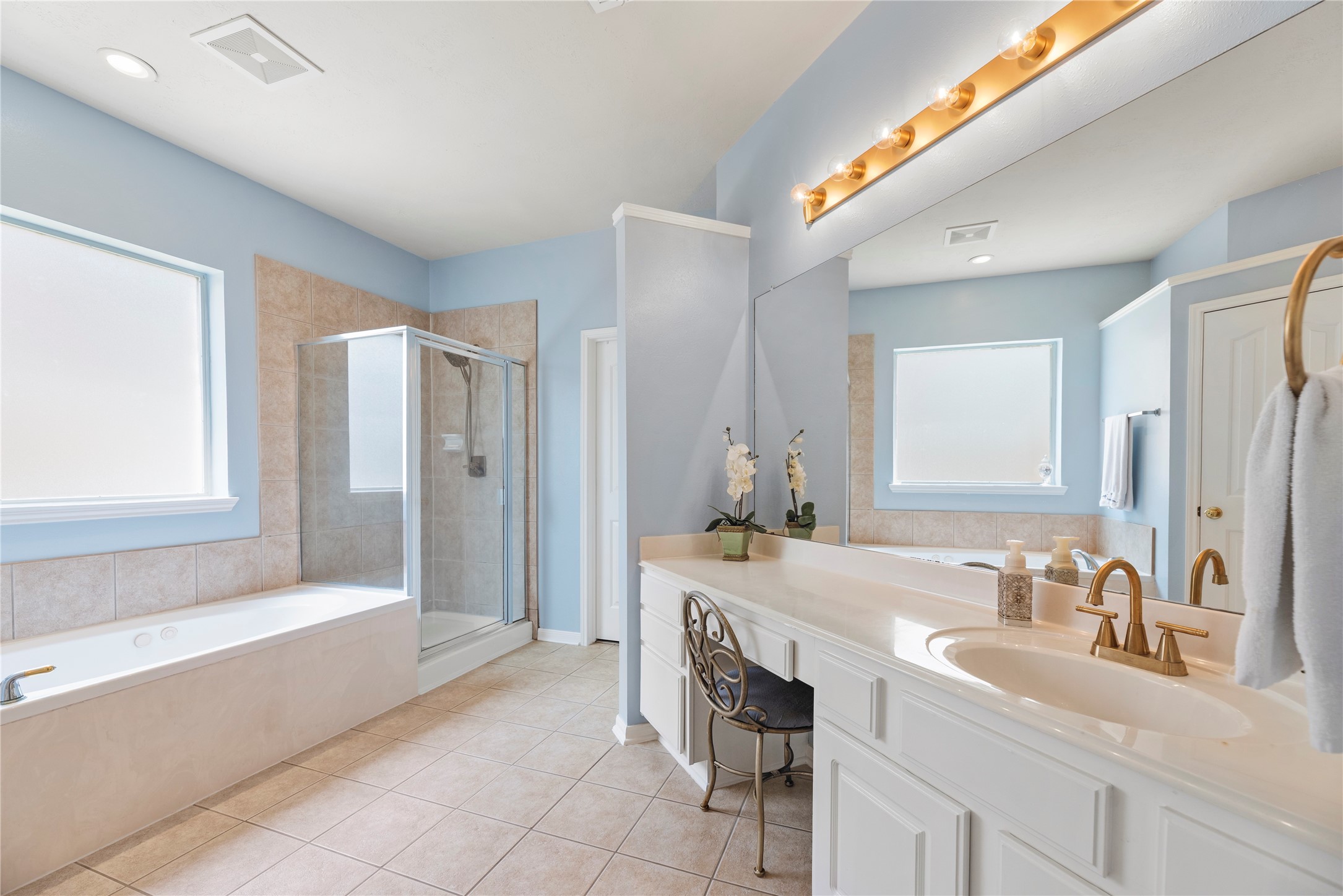 7930 Chateau Point Lane Houston, TX 77041 - Photo 17 of 34 Bright and spacious primary bathroom featuring a large jetted tub, separate glass-enclosed shower, and a double vanity with elegant fixtures. The soft blue walls and ample natural light create a peaceful atmosphere.