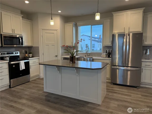 a kitchen with stainless steel appliances a refrigerator a stove a sink cabinets and a wooden floor