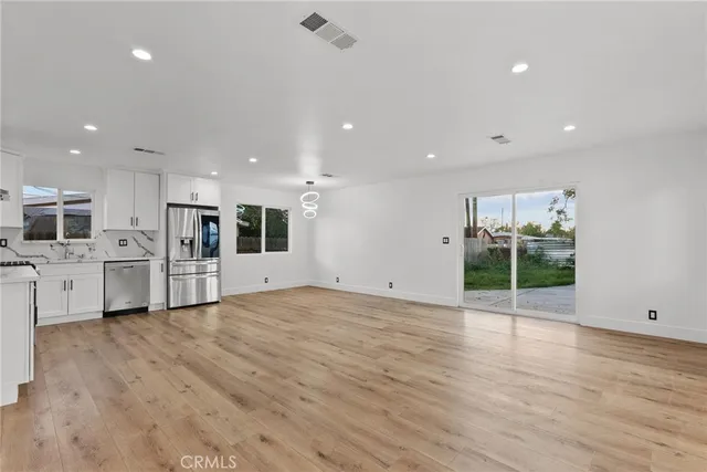 a view of an empty room with wooden floor and a kitchen