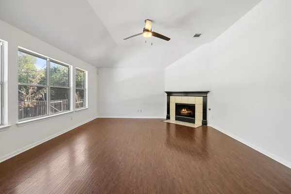 an empty room with wooden floor fireplace and windows
