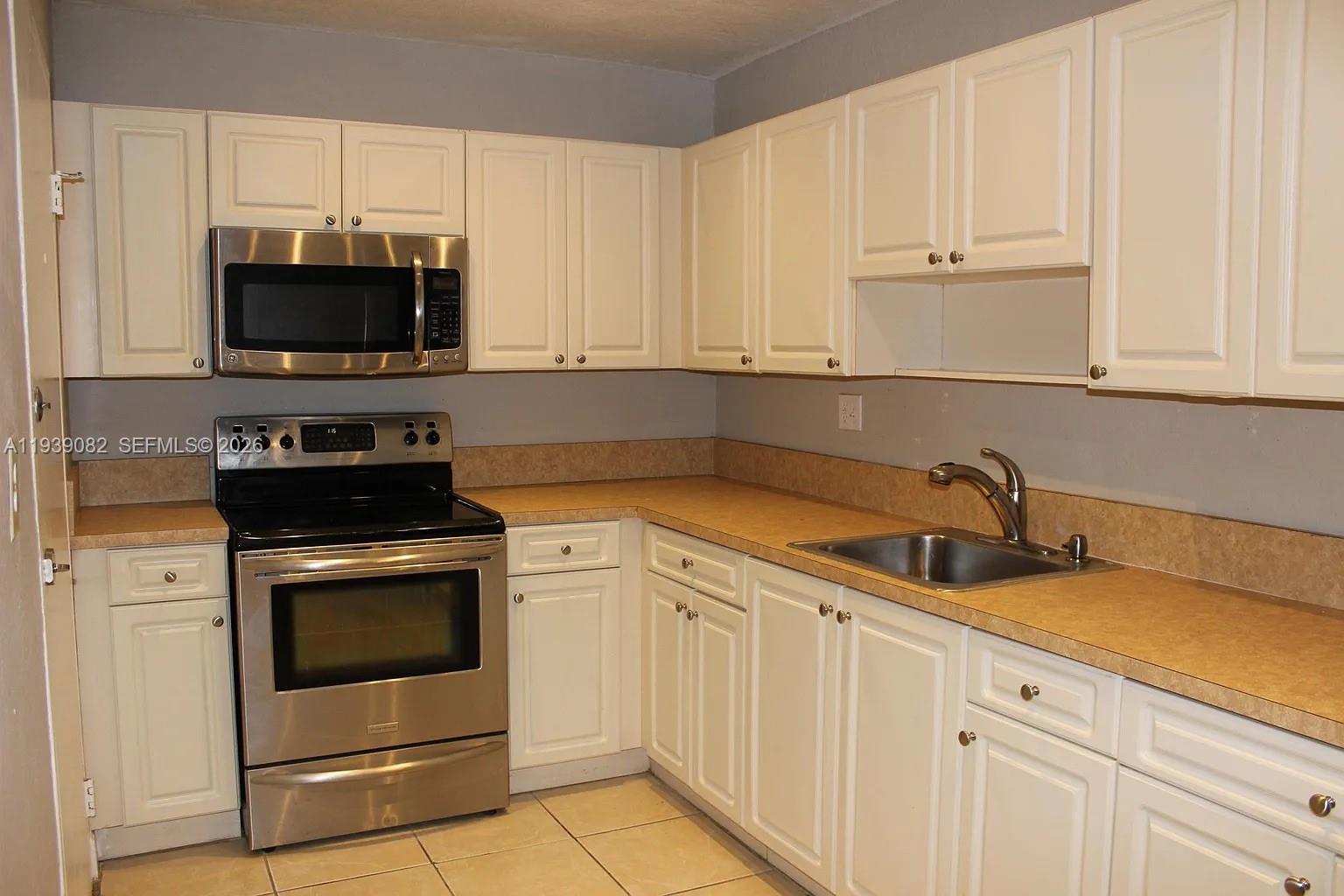 9441 Southwest 76th Street, Unit V33 Miami, FL 33173 - Photo 6 of 21 a kitchen with white cabinets and black appliances