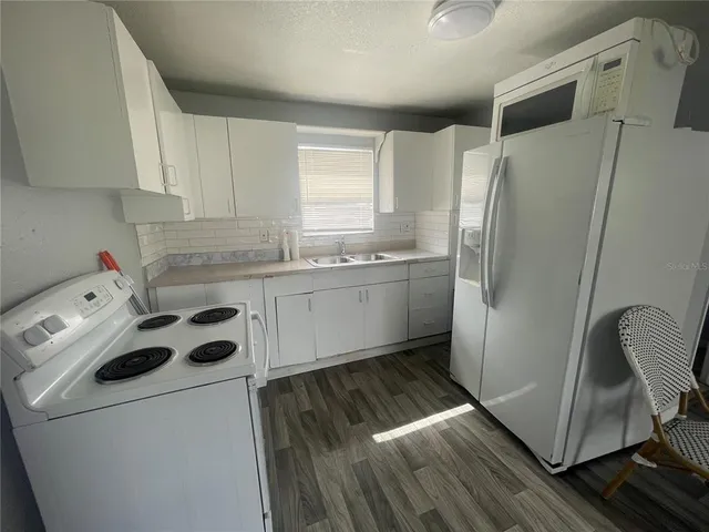 a kitchen with stainless steel appliances a refrigerator sink and white cabinets with wooden floor