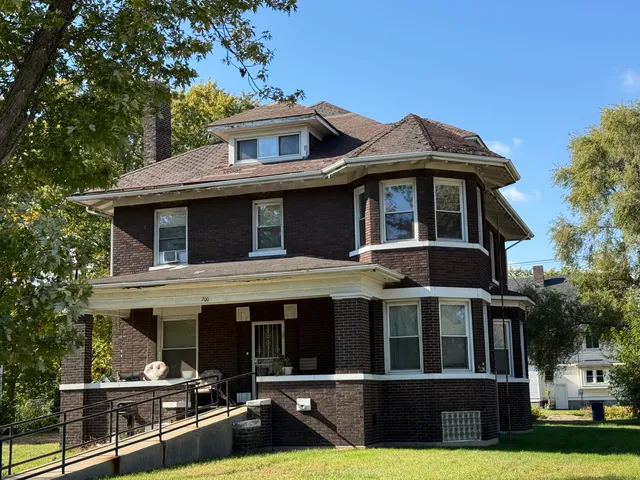 a view of a brick house with large windows and a yard with plants and large trees