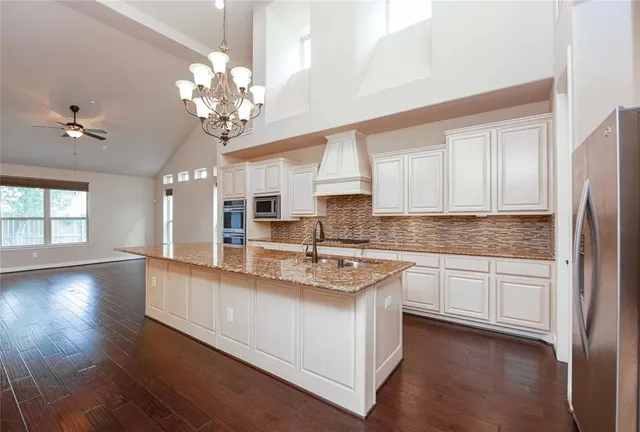 a kitchen with stainless steel appliances granite countertop a sink dishwasher a stove and a refrigerator with wooden floor