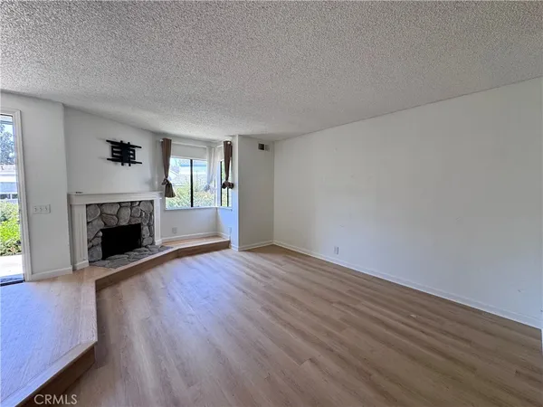 a view of an empty room with wooden floor fireplace and a window