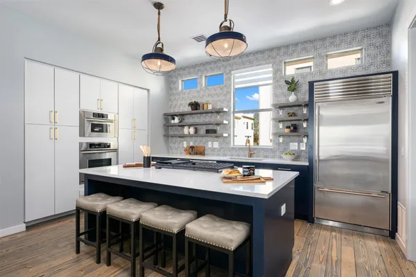 a room with stainless steel appliances kitchen island granite countertop a table chairs in it and wooden floors