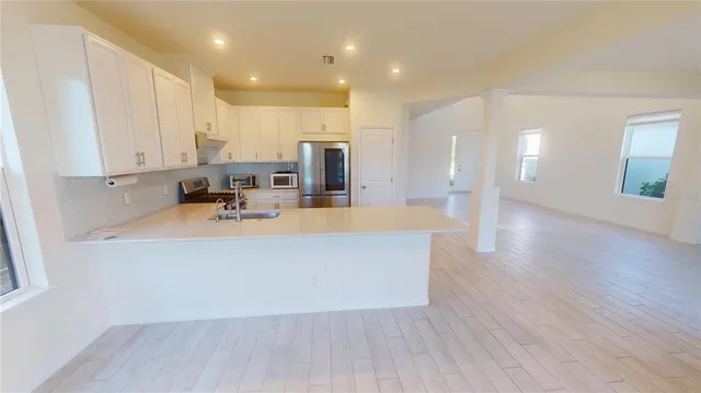 a kitchen with stainless steel appliances a refrigerator a sink a stove and white cabinets with wooden floor