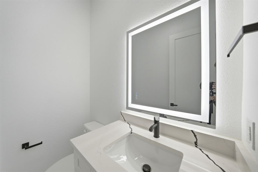 306 East 7th Street Dallas, TX 75203 - Photo 20 of 22 Modern powder room featuring a rectangular illuminated mirror, integrated sink, black faucet, white countertop with dark veining, and a white toilet