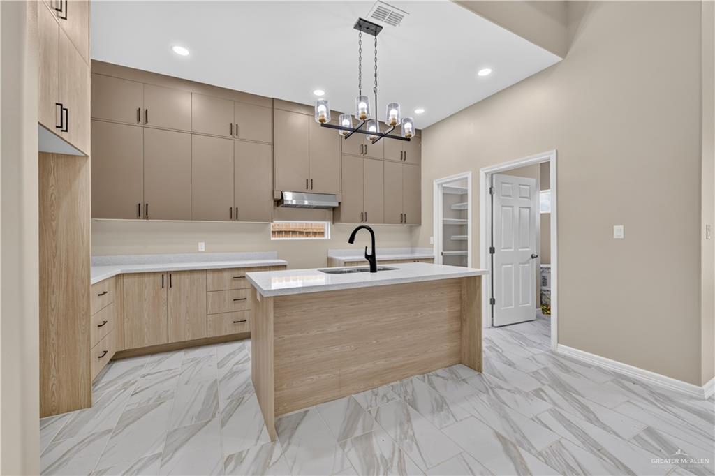 1920 Trinity Street Donna, TX 78537 - Photo 7 of 23 Spacious kitchen featuring a central island with an undermount sink, light wood-finish cabinetry, upper cabinetry in a contrasting neutral tone, white countertops, and marble-look tile flooring