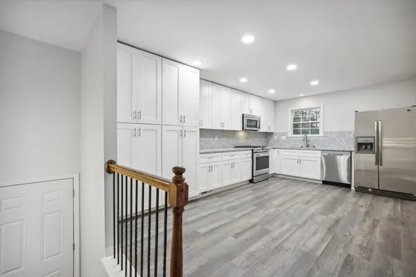 a kitchen with stainless steel appliances granite countertop a stove top oven a sink and white cabinets with wooden floor