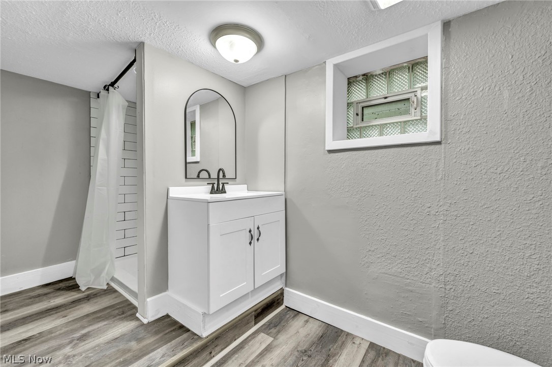 1659 Lee Road Cleveland, OH 44118 - Photo 29 of 46 White vanity with black hardware, arched mirror, black wall-mounted faucet, and wood-finish flooring