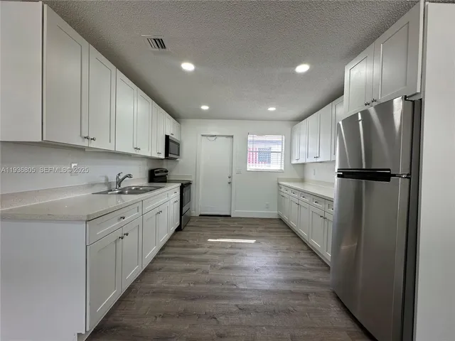 a kitchen with granite countertop a refrigerator oven a sink and white cabinets