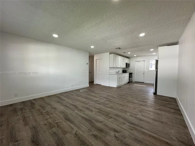 an empty room with wooden floor kitchen view and a window