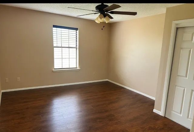 an empty room with wooden floor fan and windows