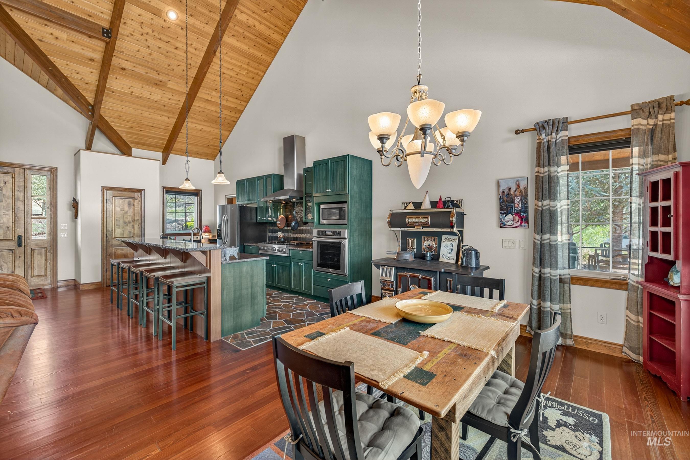 113 Deford Road White Bird, ID 83554 - Photo 8 of 49 Vaulted wood-paneled ceilings with exposed beams, wood-finish flooring, a kitchen island with seating, dark green cabinetry, and a window with exterior views
