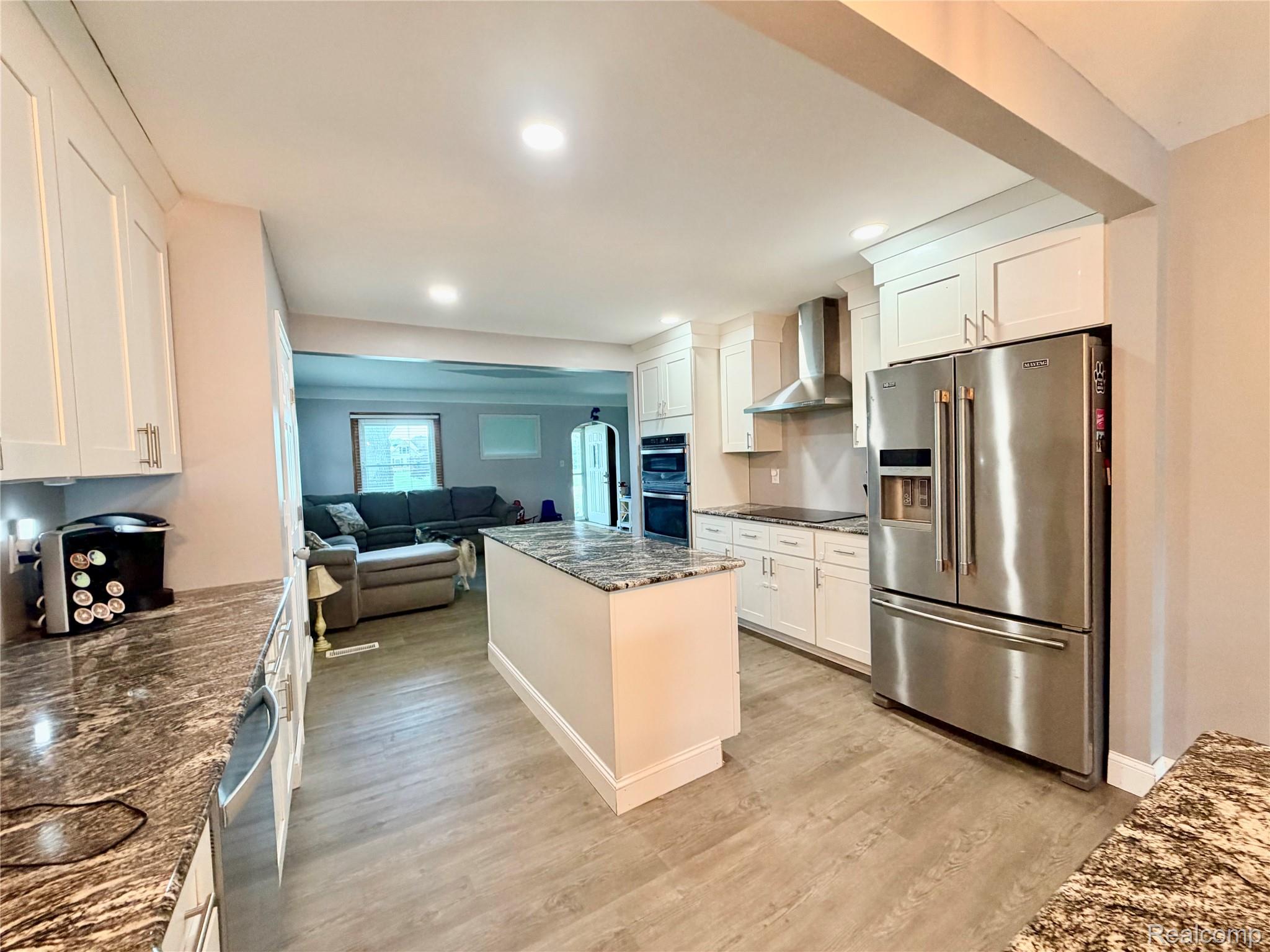 3840 East Dunbar Road Monroe, MI 48161 - Photo 20 of 38 Modern kitchen featuring a central island with a granite-style countertop, stainless steel appliances, white shaker-style cabinetry, and wood-finish flooring