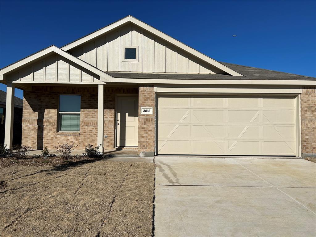 View of front of house with concrete driveway, brick siding, covered porch, and board and batten siding