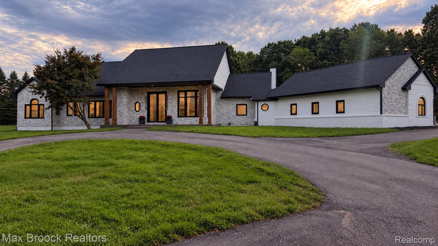 Circular driveway, light-colored brick exterior, black-framed windows, dark-colored roof, and architectural wood beam details