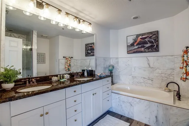 a bathroom with a double vanity sink a mirror a bathtub and next to a window