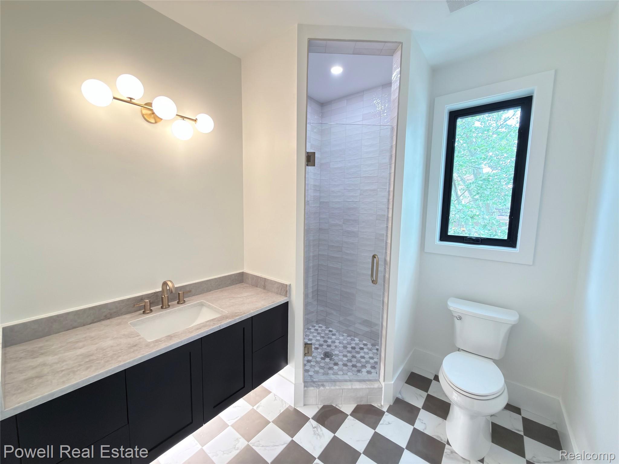 1998 Hazel Street Birmingham, MI 48009 - Photo 19 of 22 Contemporary bathroom featuring a floating vanity with a light-toned countertop, a frameless glass shower enclosure, a black-framed window, and checkered floor tiling